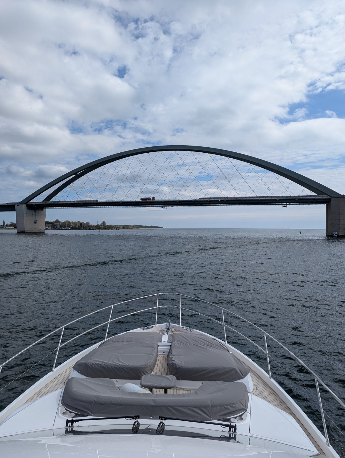 Bow of a Princess F65 motor yacht approaching a large arched road bridge on a Baltic coastal passage
