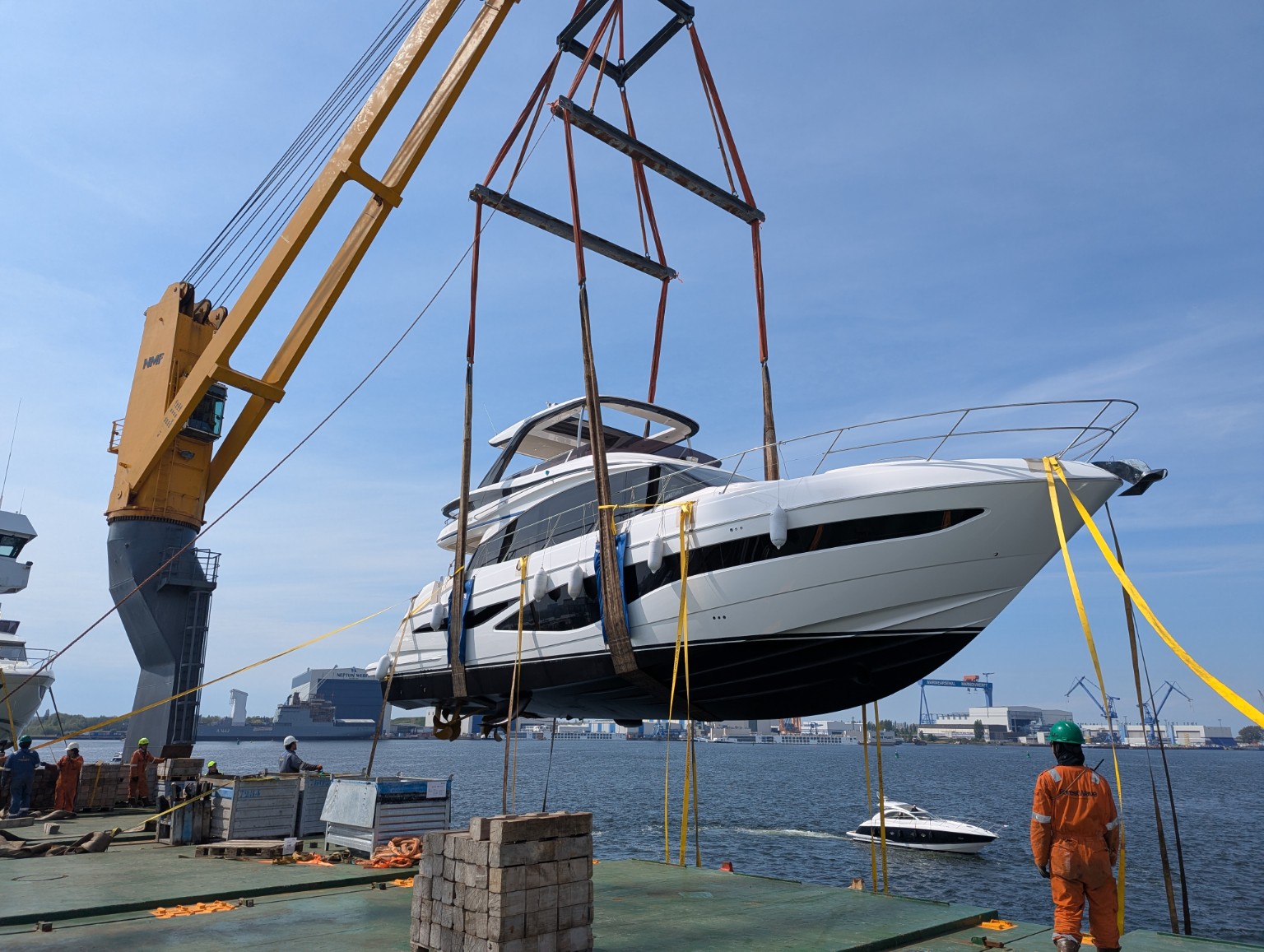 Princess F65 motor yacht suspended in slings from a harbour crane above a cargo vessel deck