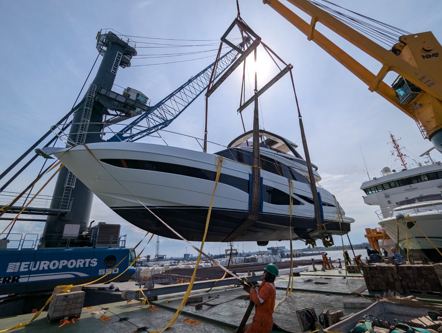 Princess F65 motor yacht lifted in slings between harbour cranes above a loading quay